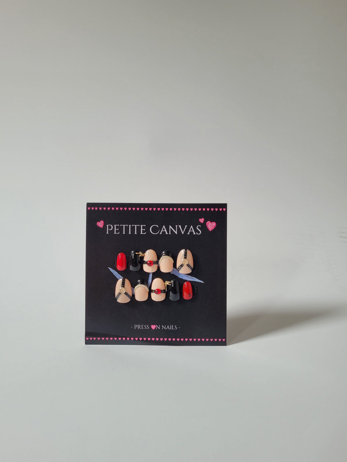 Whip-Me press-on nail set, short almond — nude, black and red nails with lace-inspired harness details, handmade by Petite Canvas