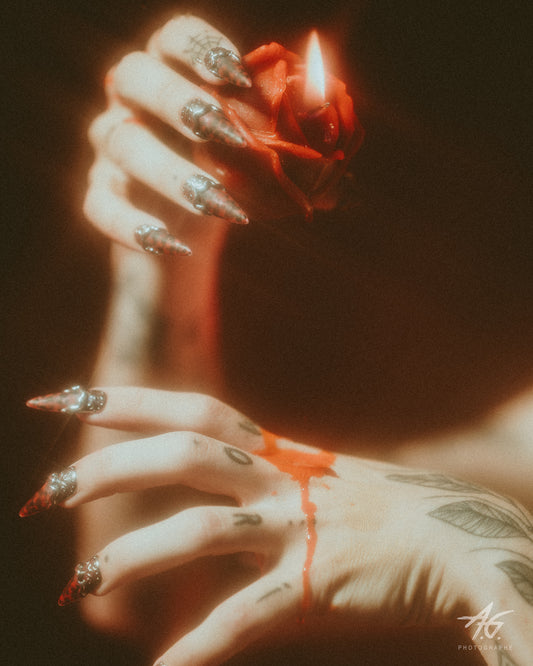It's Lilith press-on nails worn — long stiletto red and chrome nails holding a lit candle, Fetish Weekend photoshoot with Hey Miss Behave