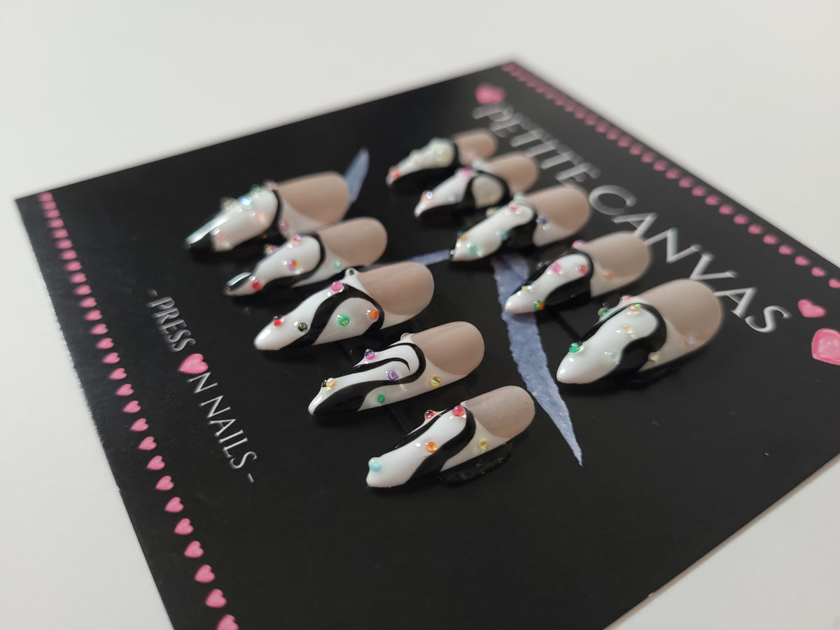 Close-up of Blinking Scene medium stiletto press-on nails — black and white french tips with colorful glass confetti