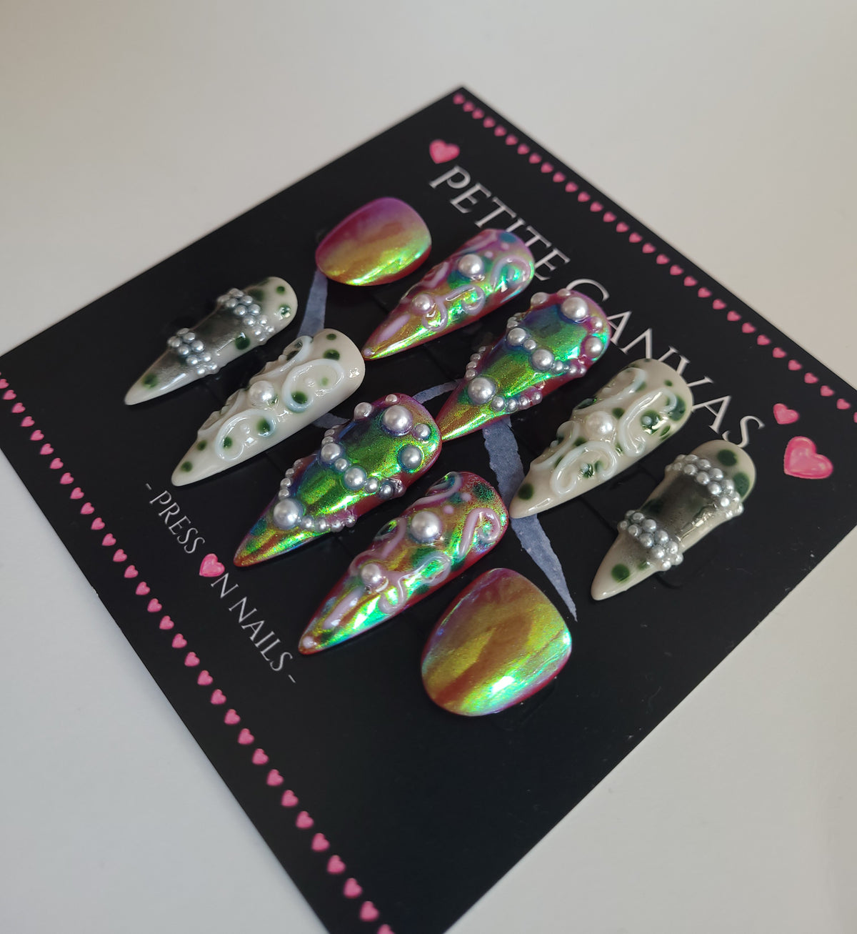 Close-up of Confessions Baroque press-on nails — iridescent green chrome, hand-painted white baroque swirls and pearls