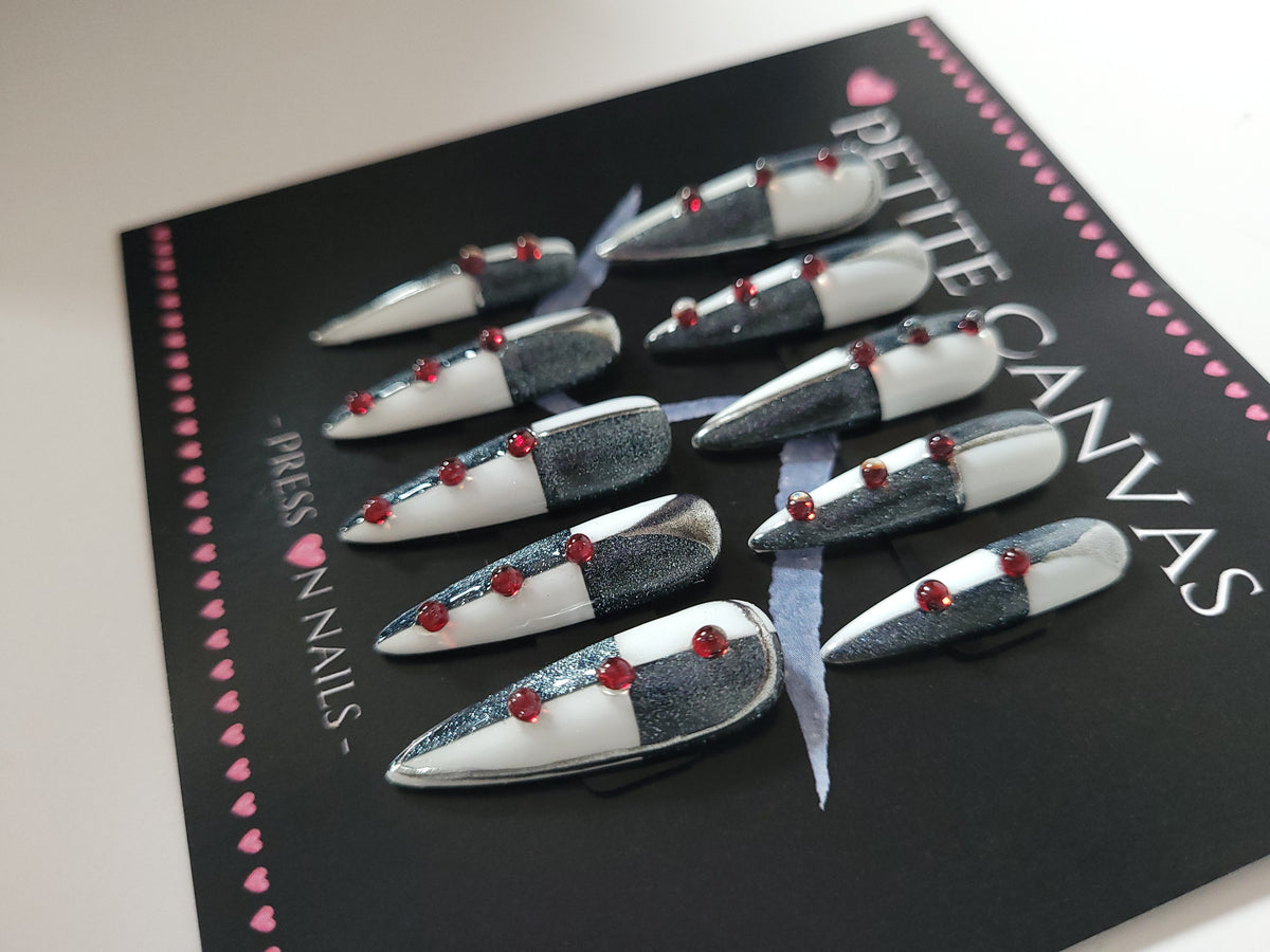 Close-up of Funambule long stiletto press-on nails — black, white and silver cat-eye with fine line work and red dots