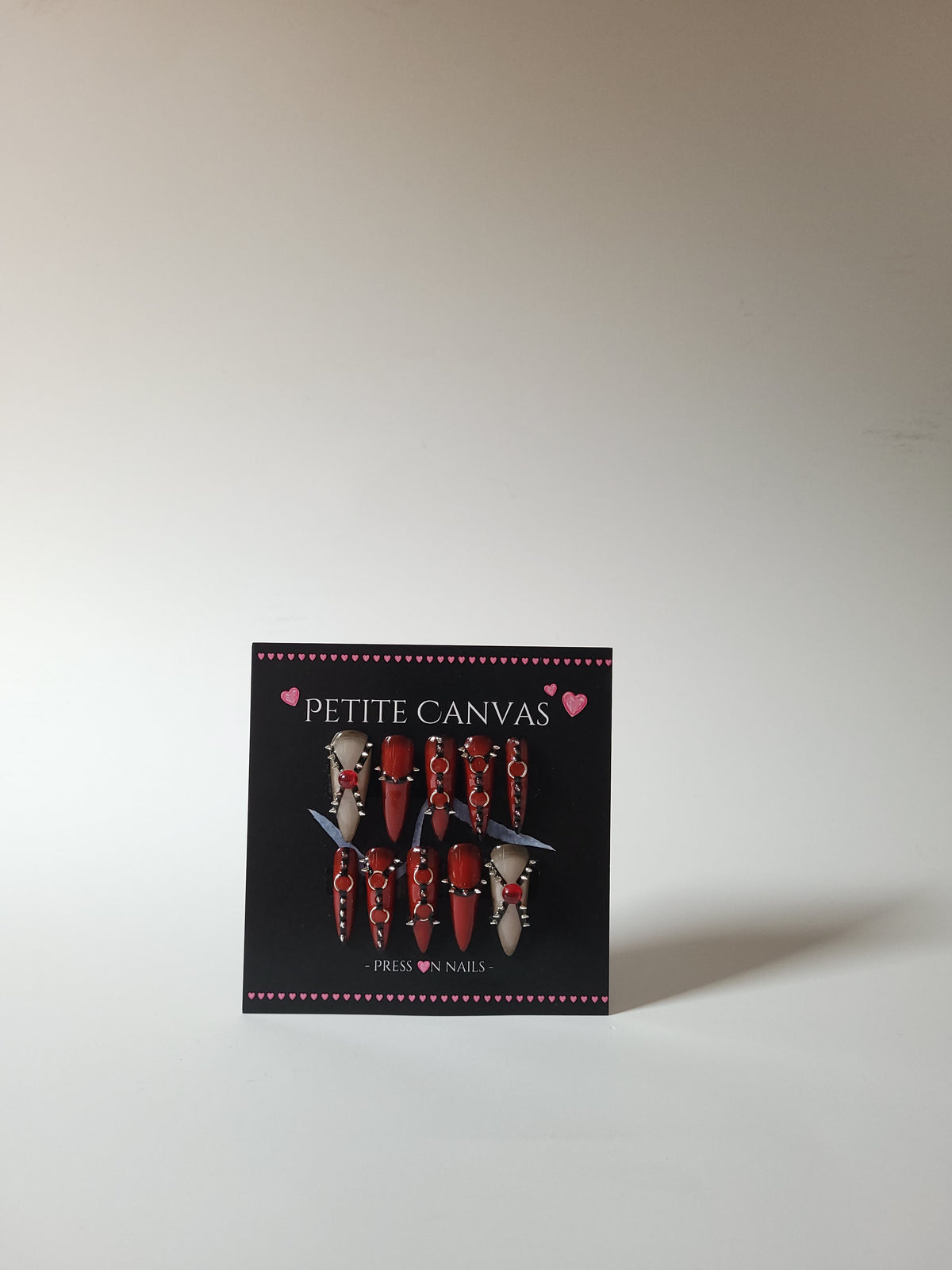 REBIRTH full press-on nail set — red and nude long stilettos with harness and spike details on display card