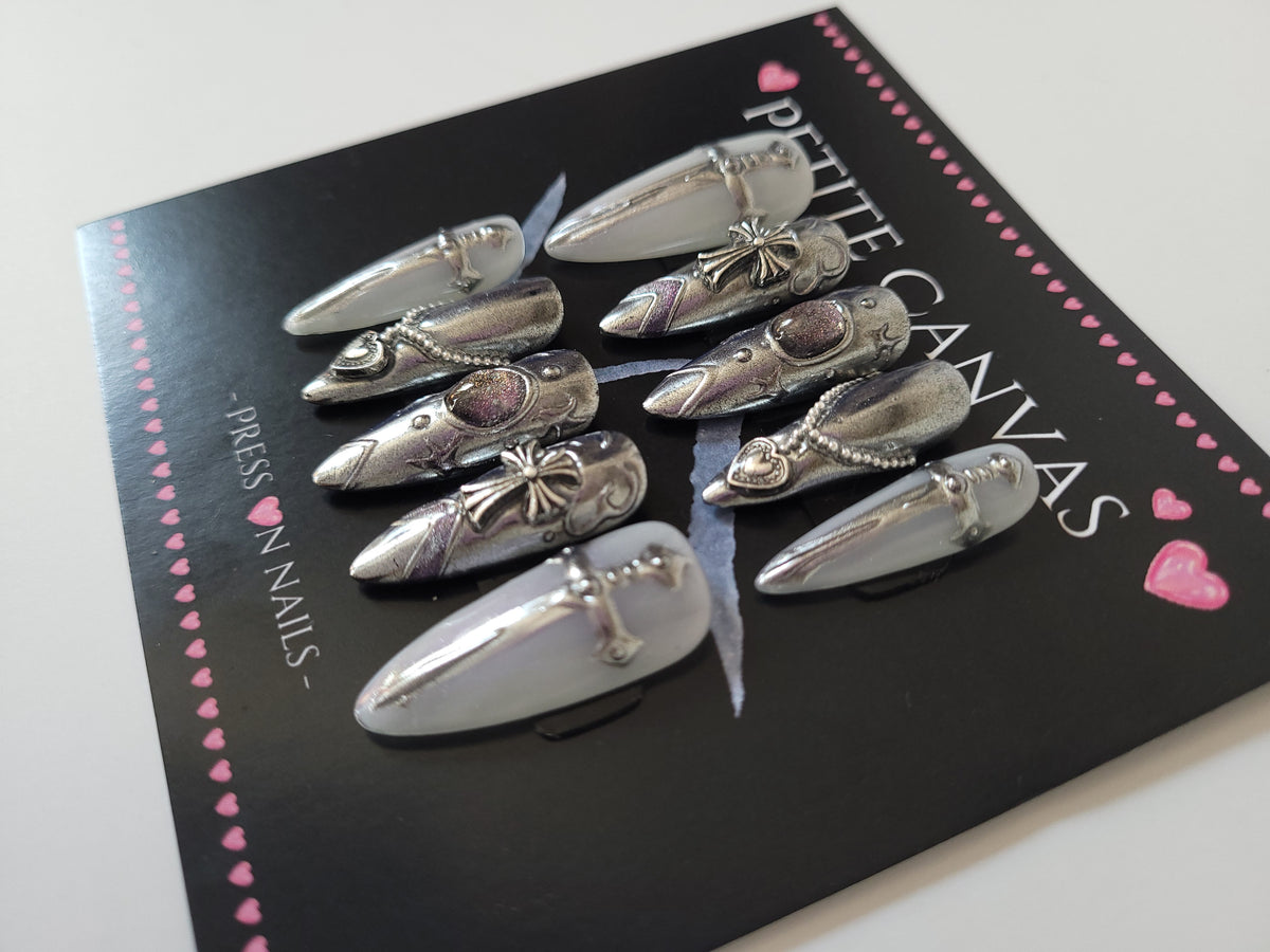 Close-up of Snow Queen long almond press-on nails — silver chrome with sword charms and filigree, cat-eye shimmer like snow on steel