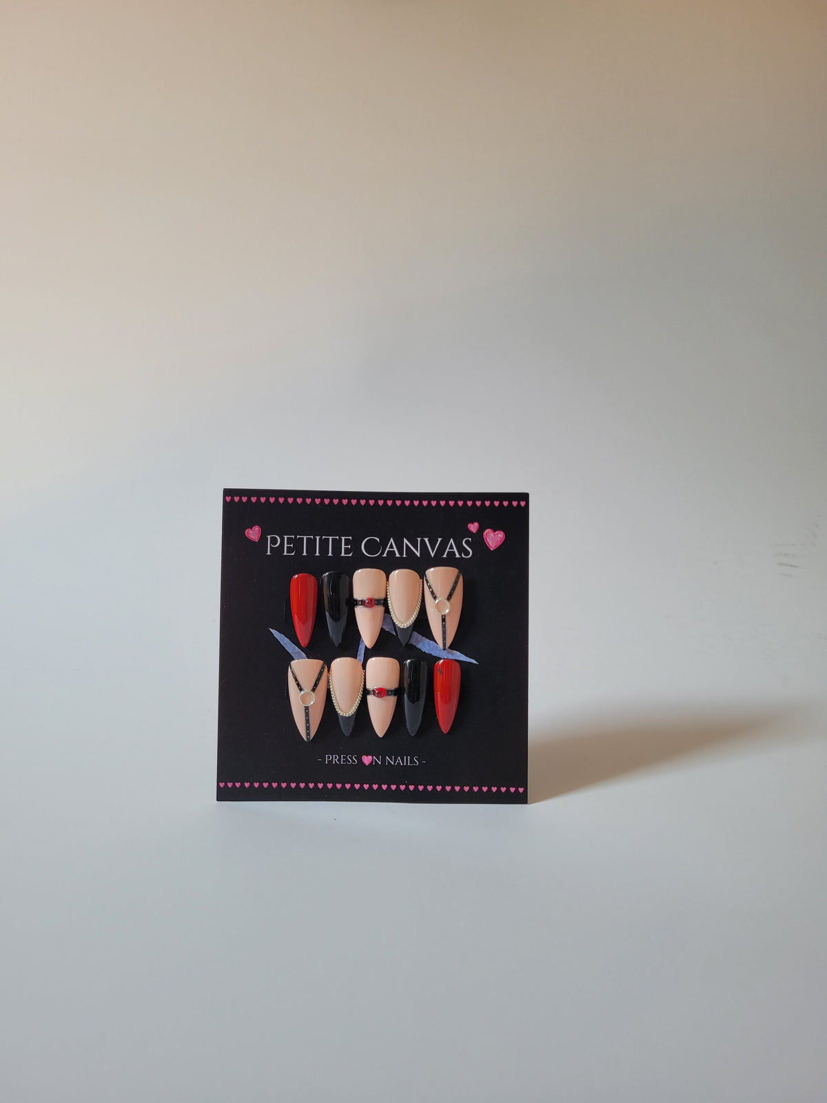 Whip-Me Red full press-on nail set on display card — harness-inspired nail art in nude, black and red